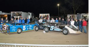 After the races on opening night at Shawano Speedway, those who were part of M.J. McBride's pit crews throughout the years assembled for a photo with the cars of Brett Swedberg and Joe Reuter. Both Swedberg and Reuter had retro M.J. graphic schemes on the right side of their cars that night. (Shawn Fredenberg photo)